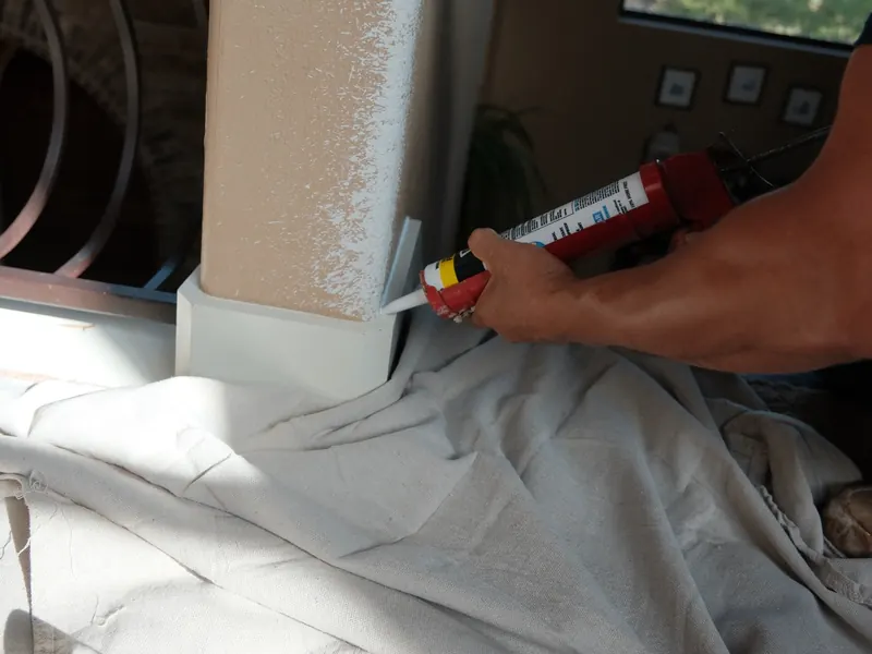 Close-up of a caulk gun sealing the joint between a baseboard and a column