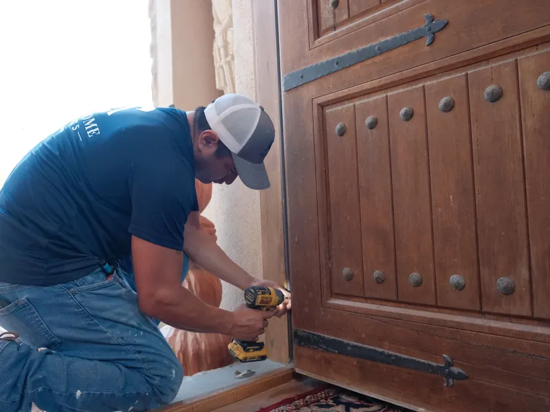 Technician using a drill to repair the hardware on a heavy wooden front door