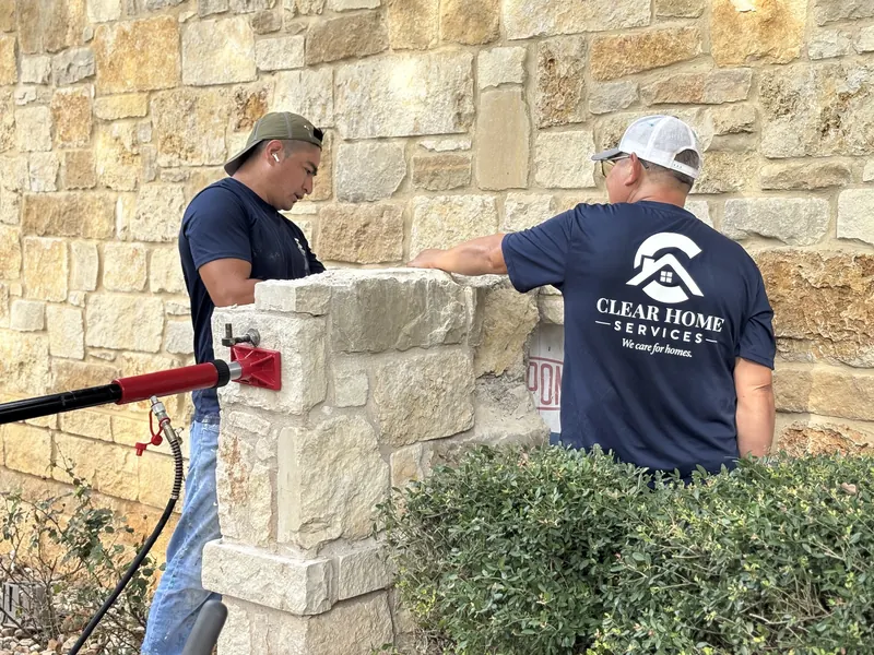 Two Clear Home Services technicians resetting limestone on a stone column beside a stone house