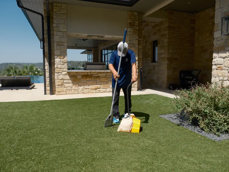 Technician clearing pet waste from a backyard lawn with a scoop and bag