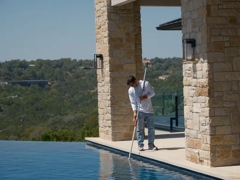 Clear Home Services technician skimming an infinity-edge pool overlooking the Texas Hill Country