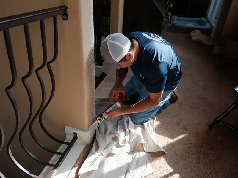 Technician working on baseboard trim at the foot of a staircase over a drop cloth