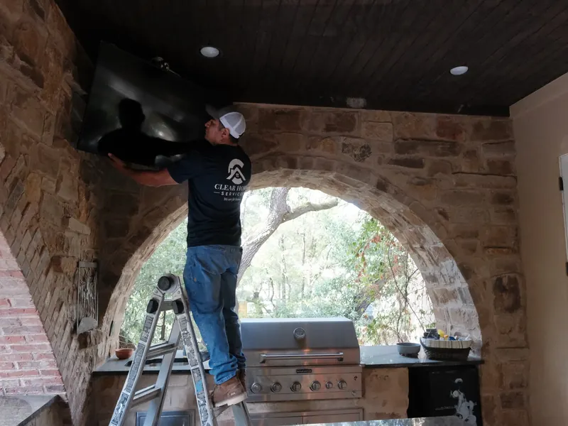 Technician on a ladder mounting a television on a stone wall in an outdoor kitchen