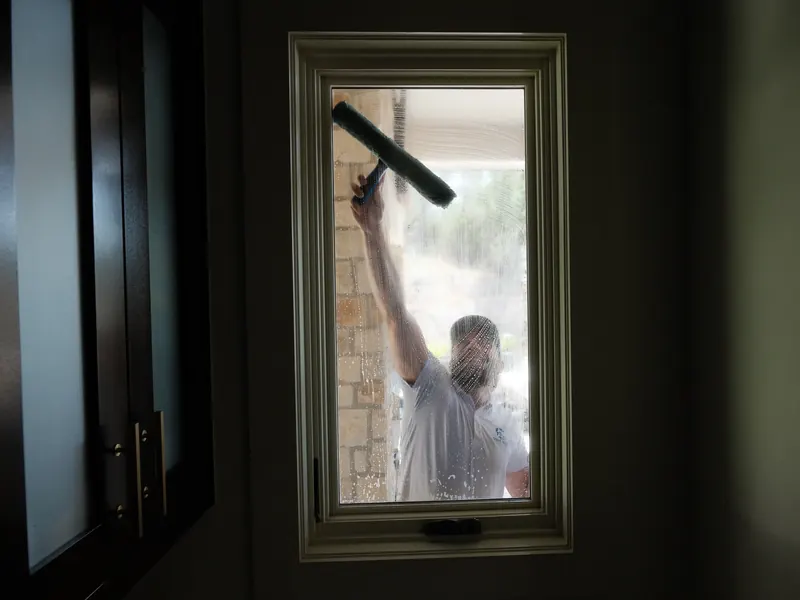 View from inside a home as a technician squeegees the exterior glass of a window